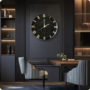 May include: A large, round wall clock with a black marble-effect face and gold Roman numerals. The clock is mounted on a dark gray wall, with a modern interior design theme. The clock's hands are gold, and the overall aesthetic is elegant and sophisticated.