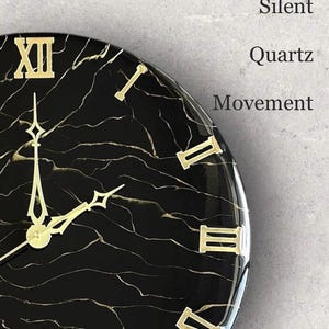 May include: A black and gold marble-patterned wall clock with gold Roman numerals and hands. The clock face features the words "Silent Quartz Movement". The clock is a decorative item for home decor.