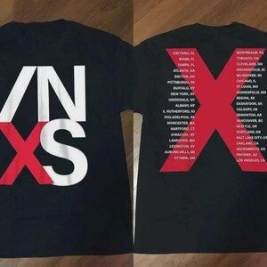 May include: Black t-shirt featuring the band name "INXS" in white and red block letters. The back of the shirt displays a large red "X" with a list of tour cities in white text.