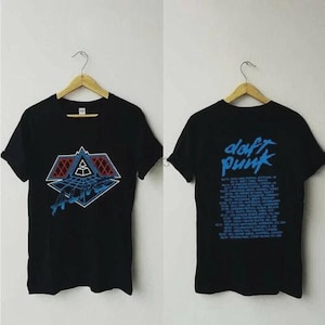 May include: Black t-shirts with a Daft Punk design. The front features a geometric design in red, blue, and white. The back of the shirt has the words "Daft Punk" in blue, along with a list of tour dates. The shirts are hanging on wooden hangers.