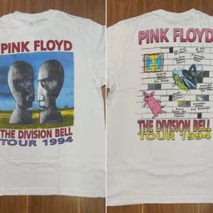 以下が含まれることがあります： ピンク・フロイドの「The Division Bell Tour 1994」デザインの白いTシャツ。前面には青い空を背景に2つの灰色の石の頭が描かれています。背面には、ピンクの豚やその他のグラフィックが描かれたレンガの壁のデザインが施されています。