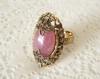 May include: A gold ring with a pink oval gemstone set in a filigree design.