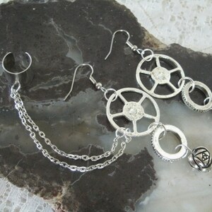 May include: A pair of silver earrings with a chain connecting them. Each earring features a circular design with a smaller circle dangling below. The smaller circle has a small ball attached to it.