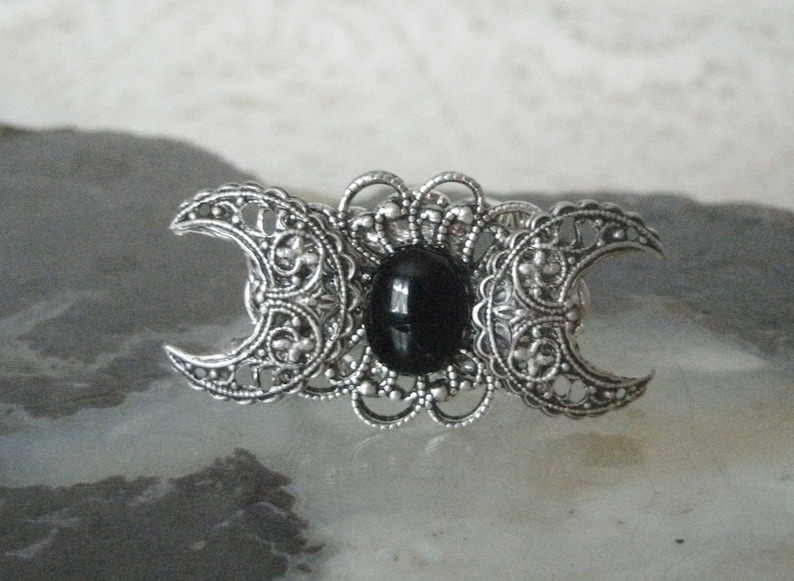 May include: Silver triple moon pendant with a black gemstone in the center.