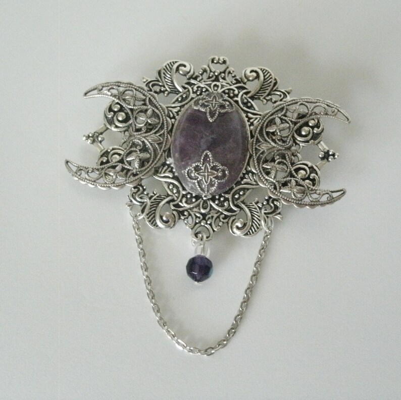 May include: Silver triple moon pendant with a purple stone and a dangling purple bead.