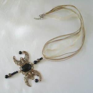 Puede incluir: Un collar artesanal con una piedra negra ovalada central y formas de media luna de filigrana. El collar tiene un dise&ntilde;o delicado con cuentas negras y un cord&oacute;n de varios hilos con cintas beige.