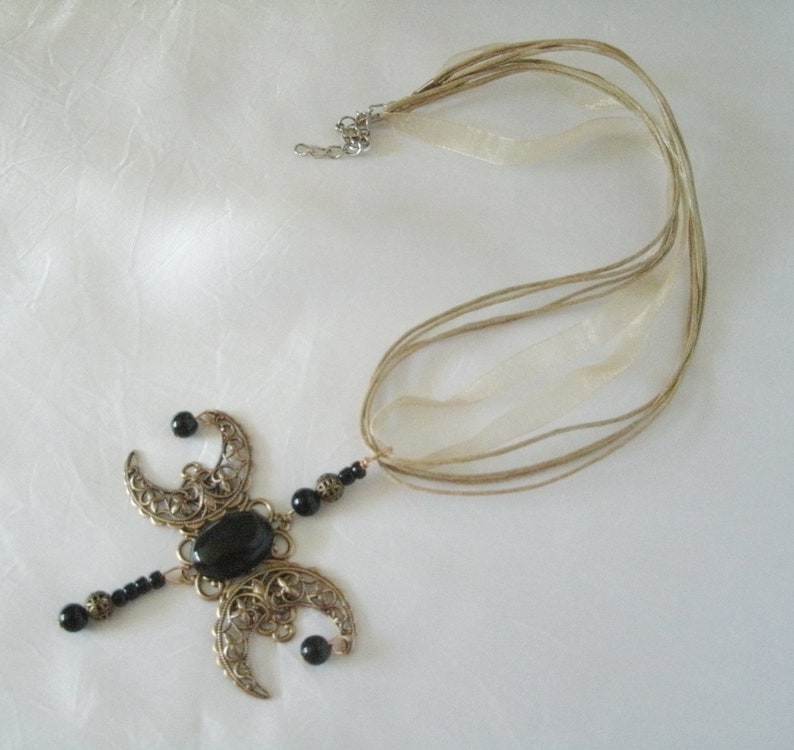 Puede incluir: Un collar artesanal con una piedra negra ovalada central y formas de media luna de filigrana. El collar tiene un dise&ntilde;o delicado con cuentas negras y un cord&oacute;n de varios hilos con cintas beige.
