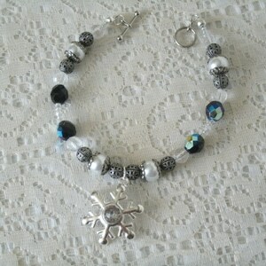 May include: A silver snowflake charm bracelet with white and black beads. The bracelet has a silver clasp and is made of clear string.
