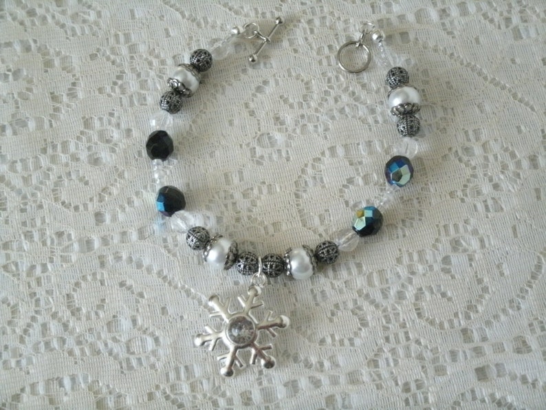 May include: A silver snowflake charm bracelet with white and black beads. The bracelet has a silver clasp and is made of clear string.