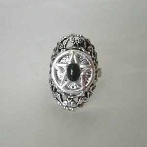 Puede incluir: Un anillo de plata con un dise&ntilde;o adornado que presenta un pentagrama negro con una piedra preciosa negra en el centro.