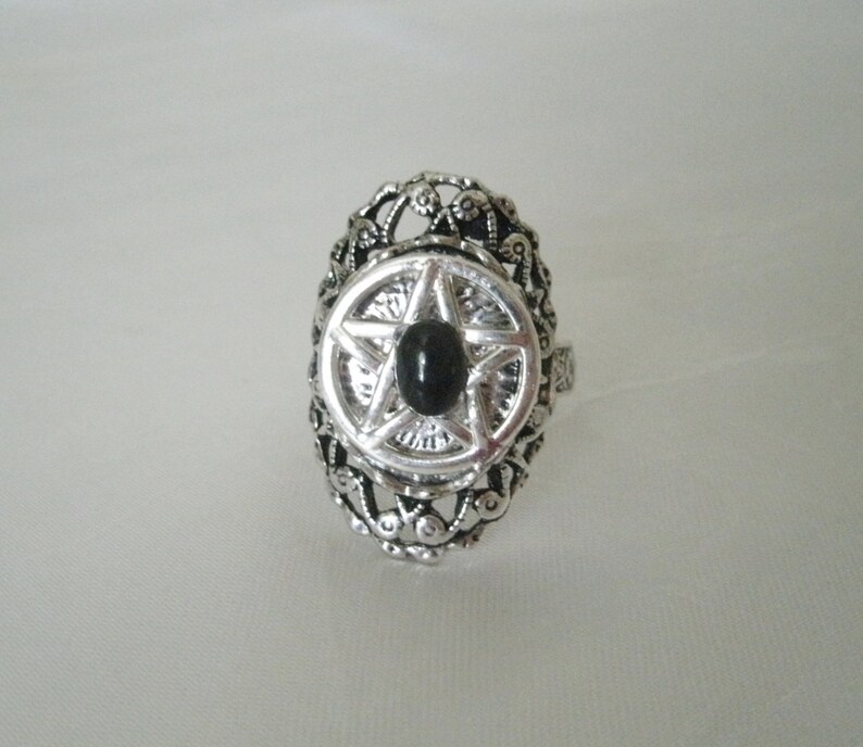 Puede incluir: Un anillo de plata con un dise&ntilde;o adornado que presenta un pentagrama negro con una piedra preciosa negra en el centro.