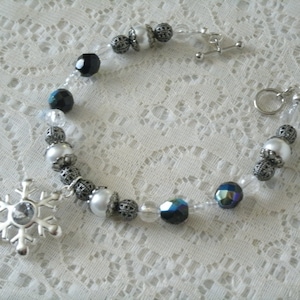 May include: A silver snowflake charm bracelet with white and black beads. The bracelet has a silver clasp and a silver chain.