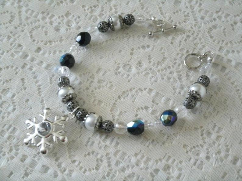 May include: A silver snowflake charm bracelet with white and black beads. The bracelet has a silver clasp and a silver chain.