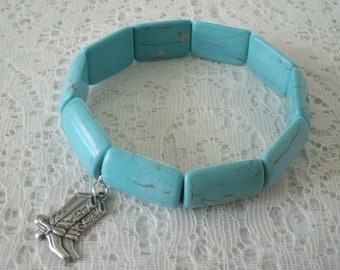 May include: A turquoise blue stretch bracelet with a silver boot charm. The bracelet is made of rectangular beads with a mottled texture.