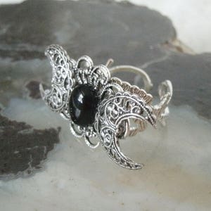 May include: Silver ring with a black stone and a triple moon design.