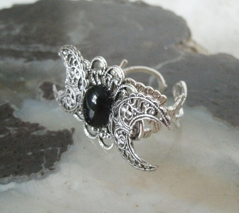 May include: Silver ring with a black stone and a triple moon design.