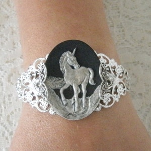 May include: Silver bracelet with a black and silver oval charm featuring a detailed unicorn design.