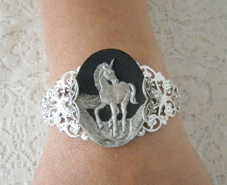 May include: Silver bracelet with a black and silver oval charm featuring a detailed unicorn design.