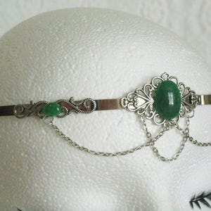 May include: Silver headband with a green gemstone and delicate chain accents.
