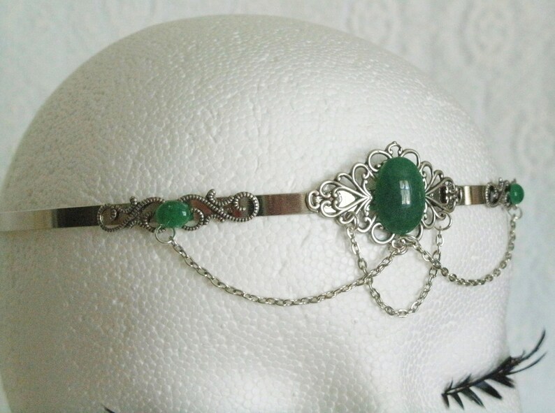 May include: Silver headband with a green gemstone and delicate chain accents.