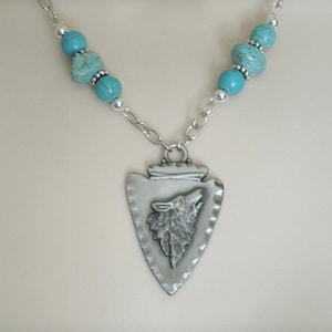 May include: A silver necklace with a turquoise bead and arrowhead pendant featuring a wolf design.