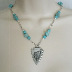 May include: A silver necklace with a turquoise bead chain and a silver arrowhead pendant with a wolf head design.
