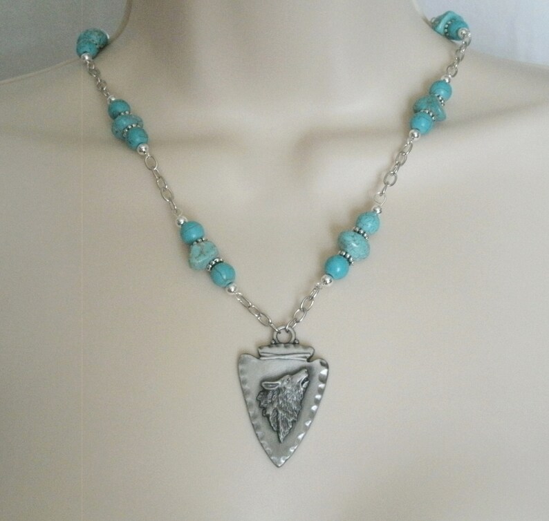 May include: A silver necklace with a turquoise bead chain and a silver arrowhead pendant with a wolf head design.