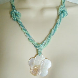 May include: A necklace made of twisted turquoise and white beads with a large white shell flower pendant.