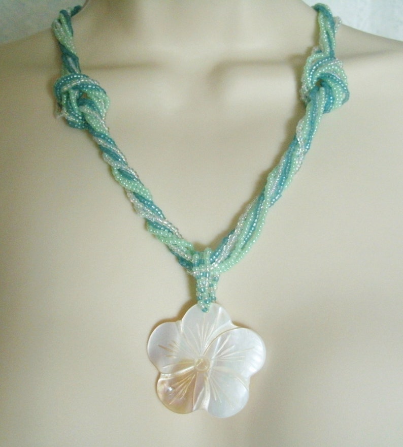 May include: A necklace made of twisted turquoise and white beads with a large white shell flower pendant.