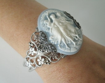 May include: A silver filigree cuff bracelet with a blue cameo featuring a white sculpted design of three women dancing.