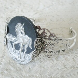 May include: A silver bracelet with a black cameo featuring a silver unicorn. The bracelet has a delicate filigree design.