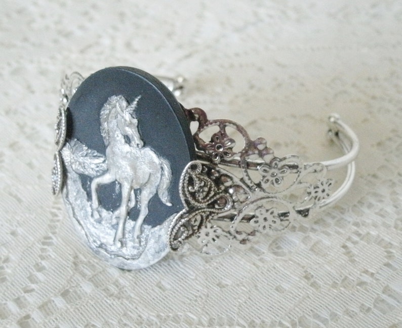 May include: A silver bracelet with a black cameo featuring a silver unicorn. The bracelet has a delicate filigree design.