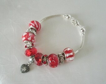 Puede incluir: Un brazalete de plata con cuentas de vidrio rojo y blanco y un dije de corazón de plata.