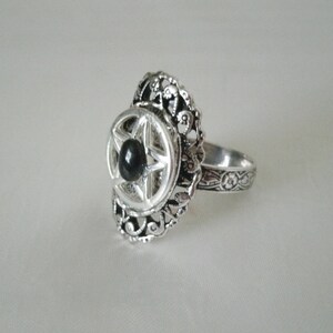 Puede incluir: Un anillo de plata con una piedra negra engastada en un dise&ntilde;o en forma de estrella. El anillo tiene una banda detallada y adornada.