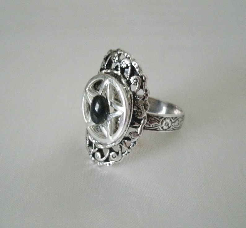 Puede incluir: Un anillo de plata con una piedra negra engastada en un dise&ntilde;o en forma de estrella. El anillo tiene una banda detallada y adornada.
