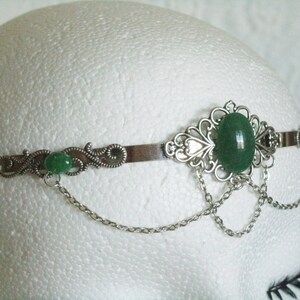 May include: Silver headband with a green gemstone and delicate chain accents.