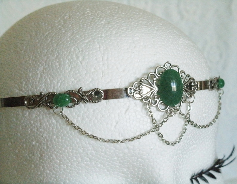 May include: Silver headband with a green gemstone and delicate chain accents.