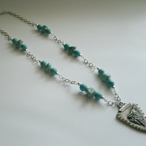 May include: A silver chain necklace with turquoise beads and a silver arrowhead pendant. The arrowhead has a detailed design.