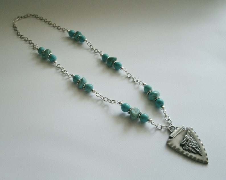 May include: A silver chain necklace with turquoise beads and a silver arrowhead pendant. The arrowhead has a detailed design.