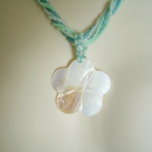 May include: A white shell flower pendant necklace with a green and blue beaded chain.