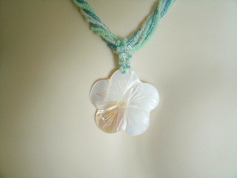 May include: A white shell flower pendant necklace with a green and blue beaded chain.
