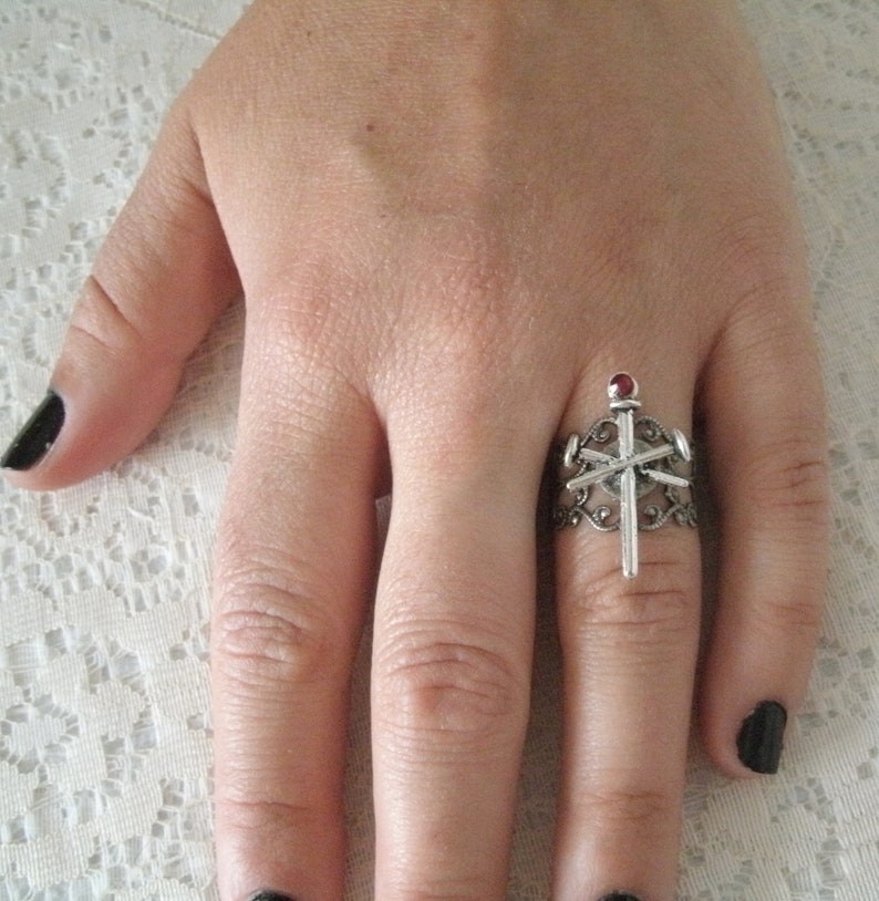 May include: A silver ring with a red stone and a silver cross design.