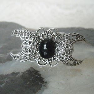 May include: A silver triple moon ring with a black onyx gemstone in the center. The ring features intricate filigree details and a crescent moon design.