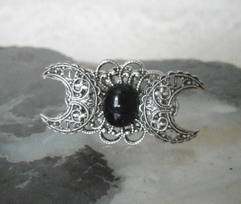 May include: A silver triple moon ring with a black onyx gemstone in the center. The ring features intricate filigree details and a crescent moon design.
