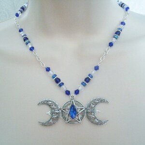 May include: A silver necklace featuring a triple moon pendant with a blue crystal at its centre. The necklace is crafted with a silver chain and blue and clear beads.