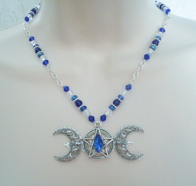 May include: A silver necklace featuring a triple moon pendant with a blue crystal at its centre. The necklace is crafted with a silver chain and blue and clear beads.