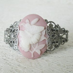 May include: A silver filigree bracelet with a pink cameo featuring a white butterfly design.