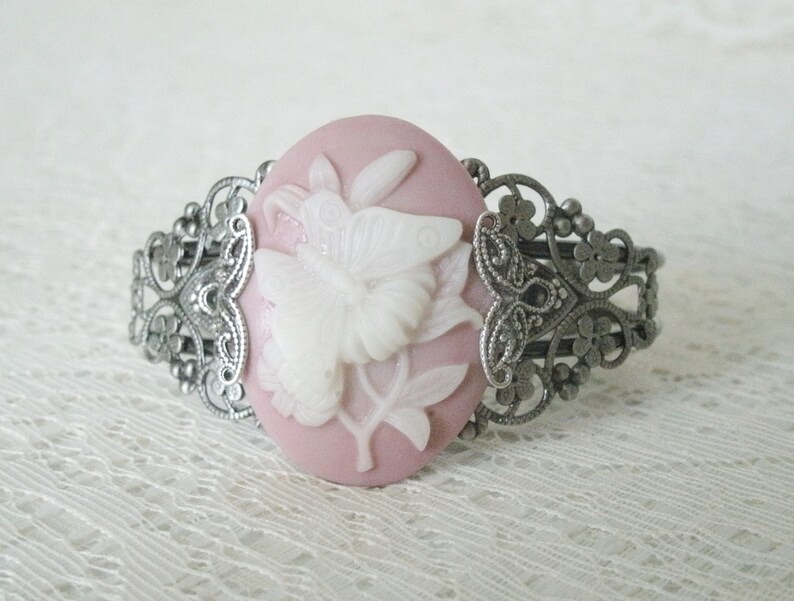 May include: A silver filigree bracelet with a pink cameo featuring a white butterfly design.