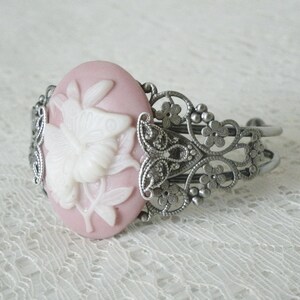 May include: A silver filigree bracelet with a pink cameo featuring a white butterfly design.