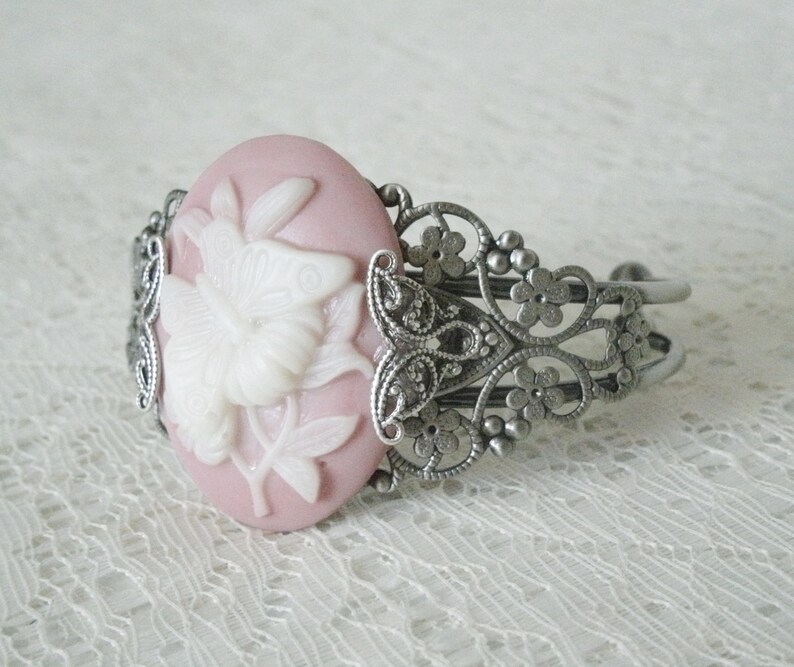 May include: A silver filigree bracelet with a pink cameo featuring a white butterfly design.
